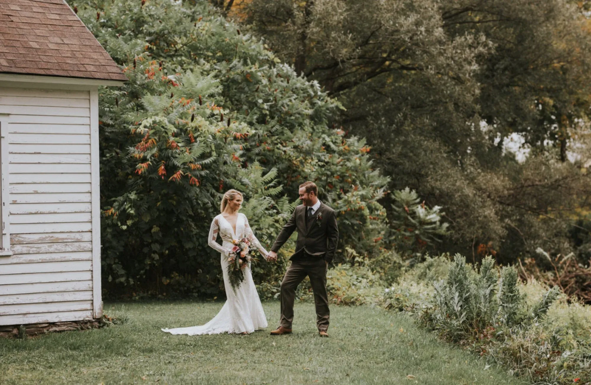 A bride and groom walking hand in hand in the backyard at Book Village Inn